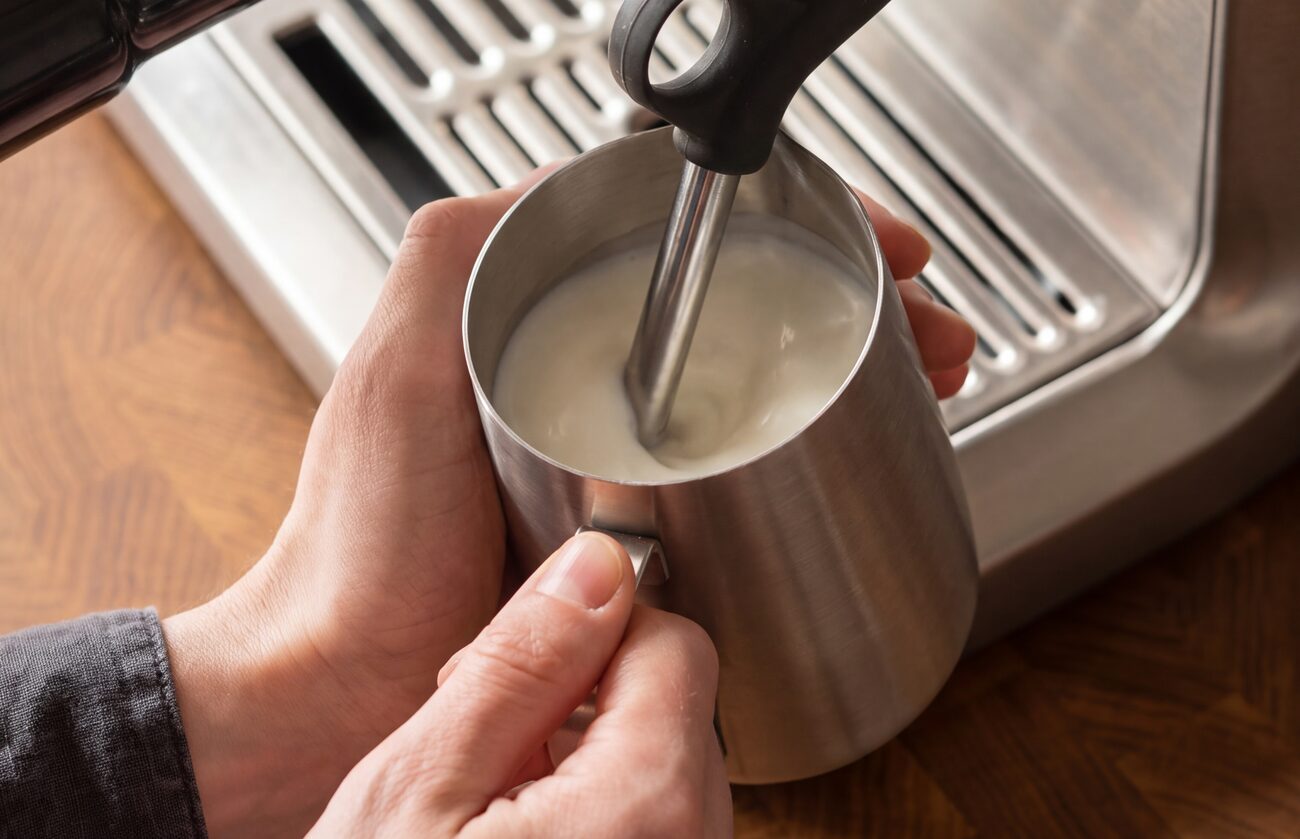 Melk stomen met de stoompijp van de Sage Barista Express, de kan half gevuld met microfoam