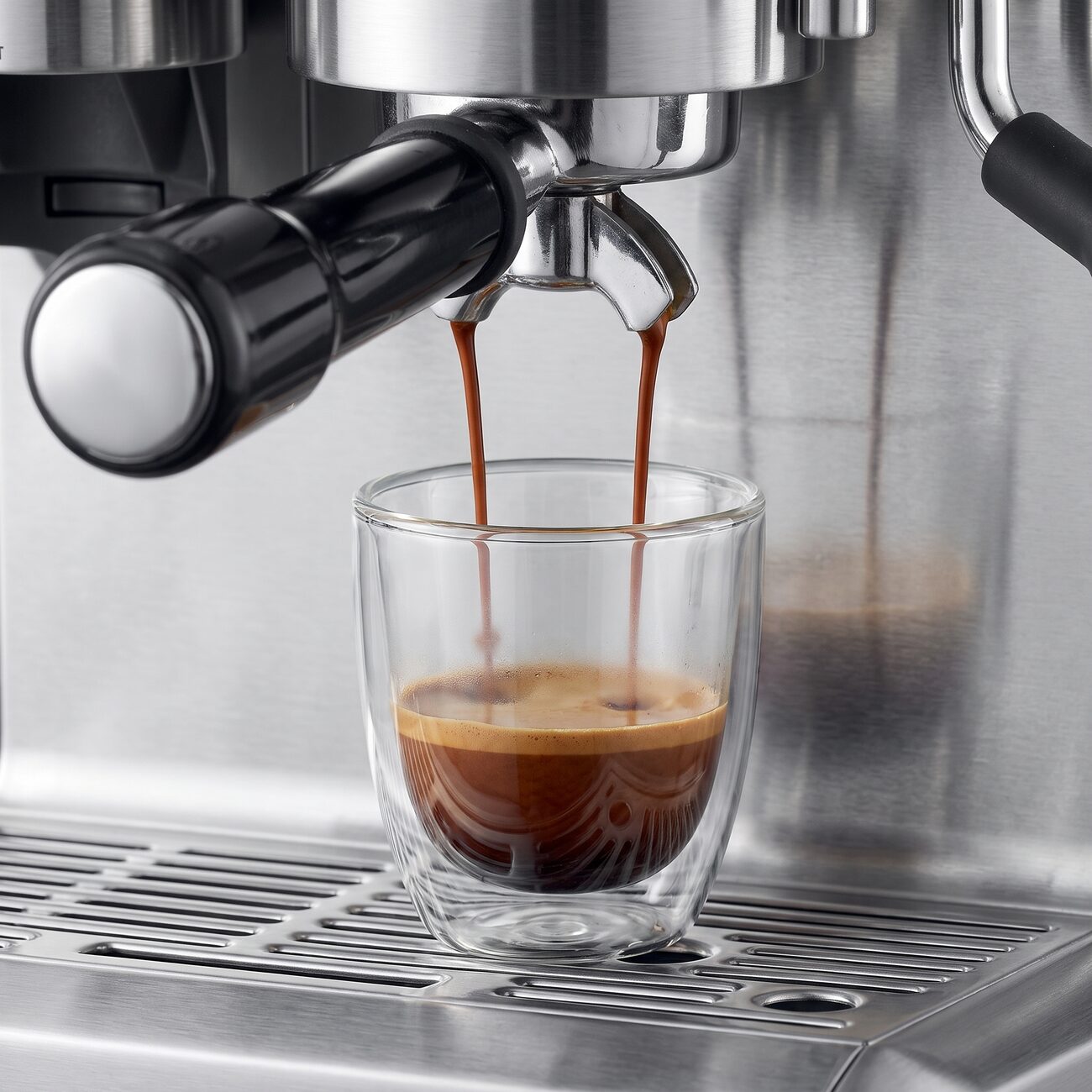 De dubbele uitloop van de Sage Barista Express trekt een shot in een dubbelwandig glaasje